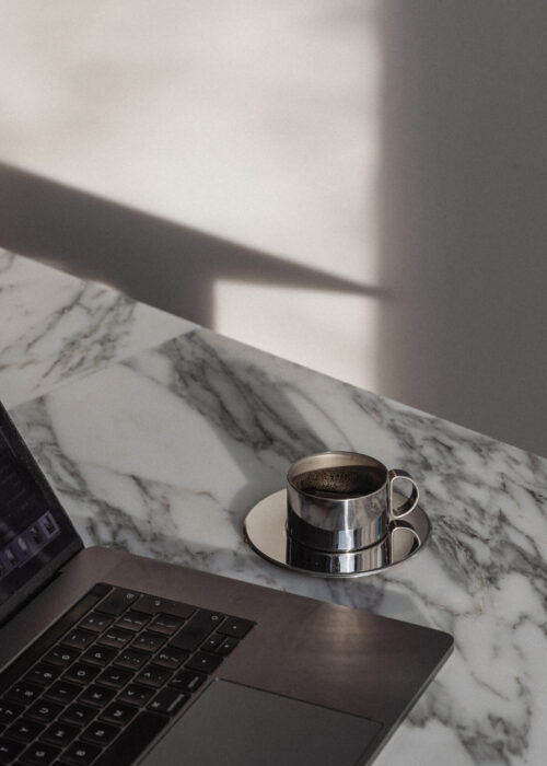 Ordenador portátil y taza sobre una mesa de mármol iluminada por luz natural.