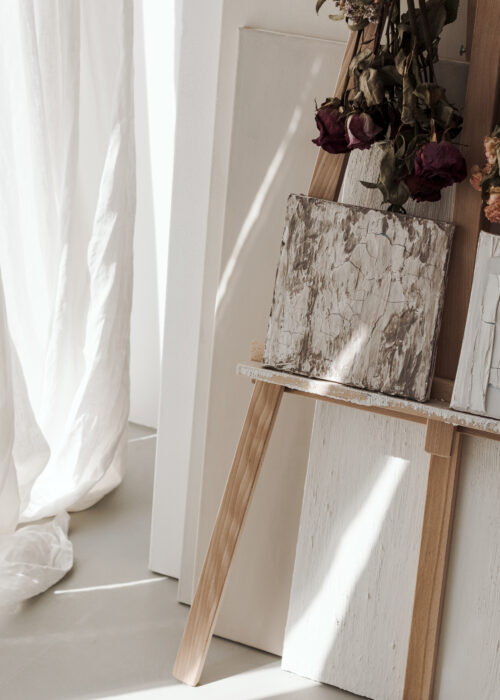 Caballete con muestras de materiales junto a una ventana con cortinas blancas.
