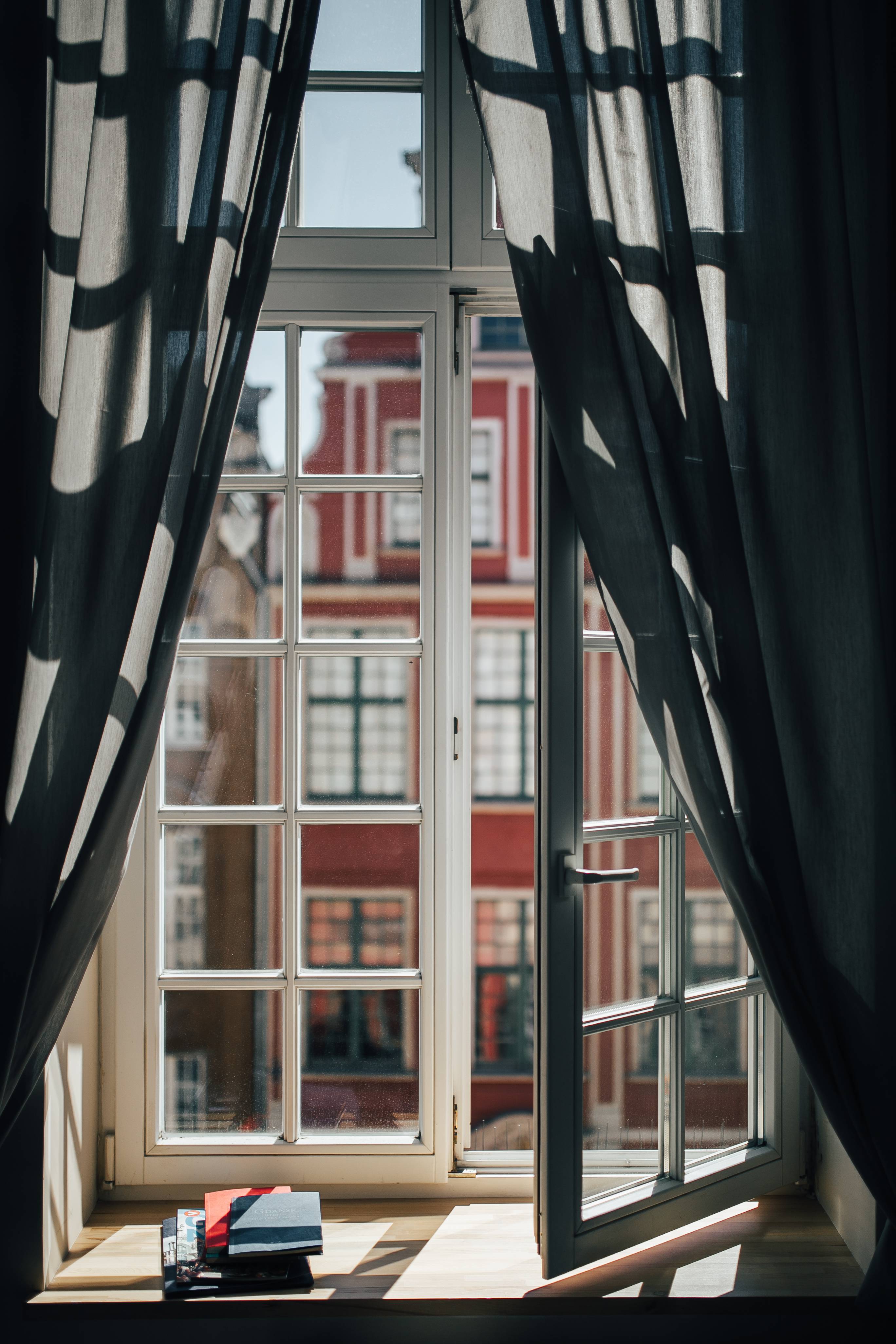 Ventana abierta con luz natural y vistas a una fachada residencial: una mirada desde el interior hacia el barrio.