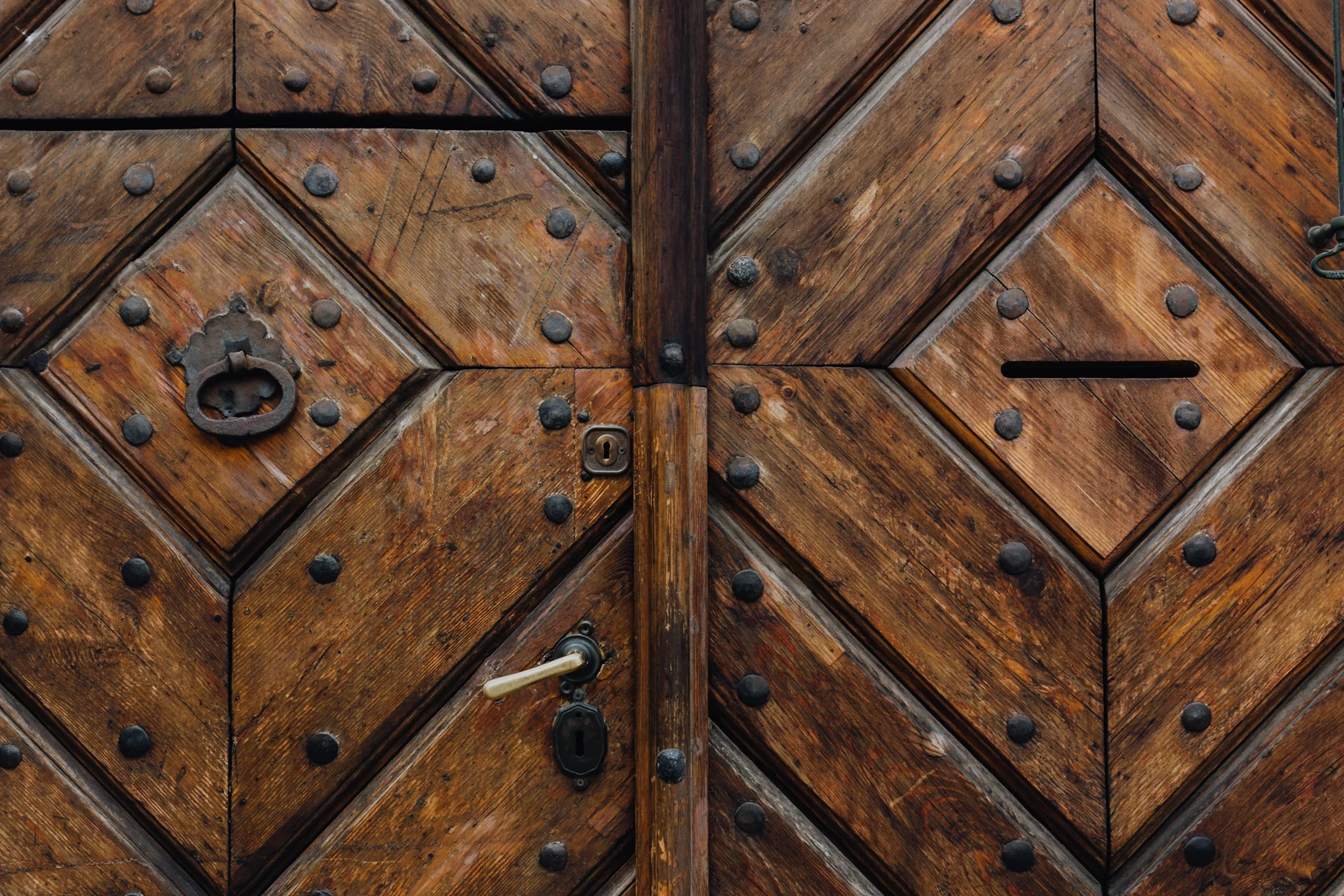 Detalle de madera envejecida, aldaba de hierro y herrajes en una puerta antigua.
