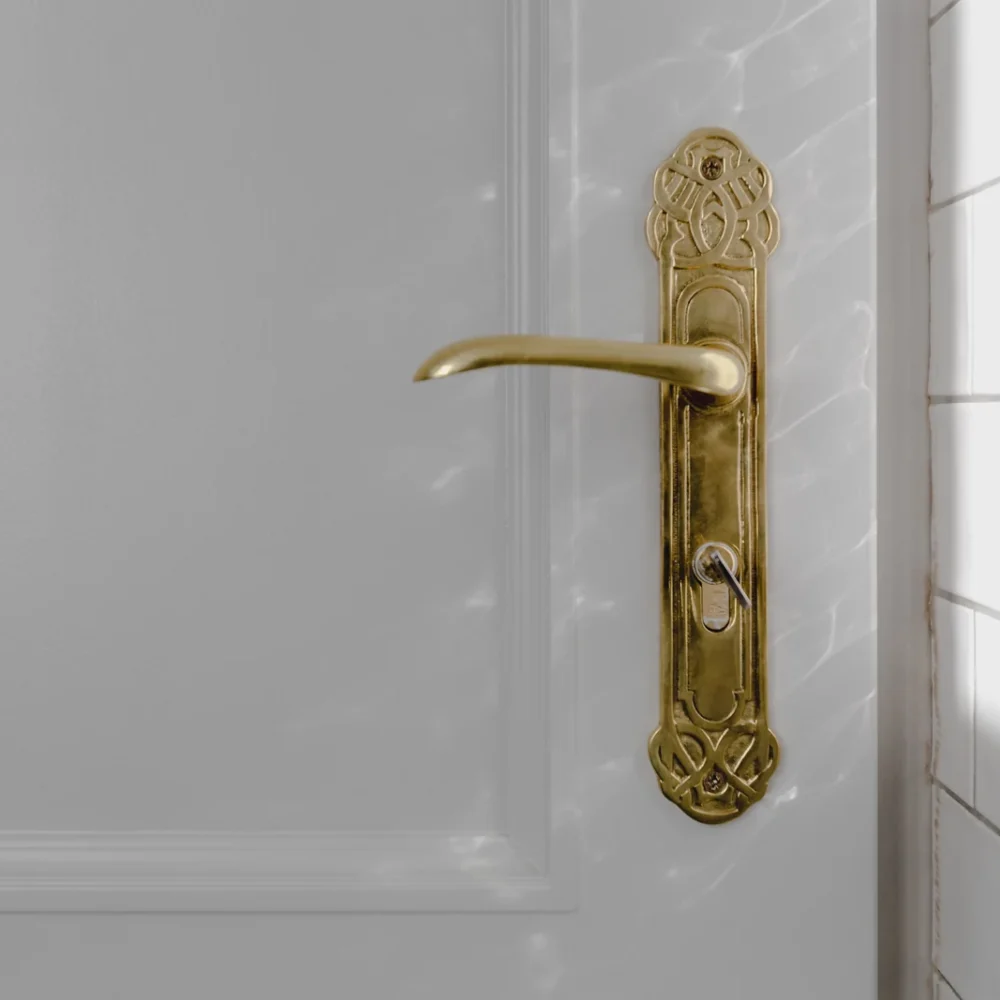 Manilla antigua de latón sobre una puerta blanca, iluminada por la luz de una ventana.