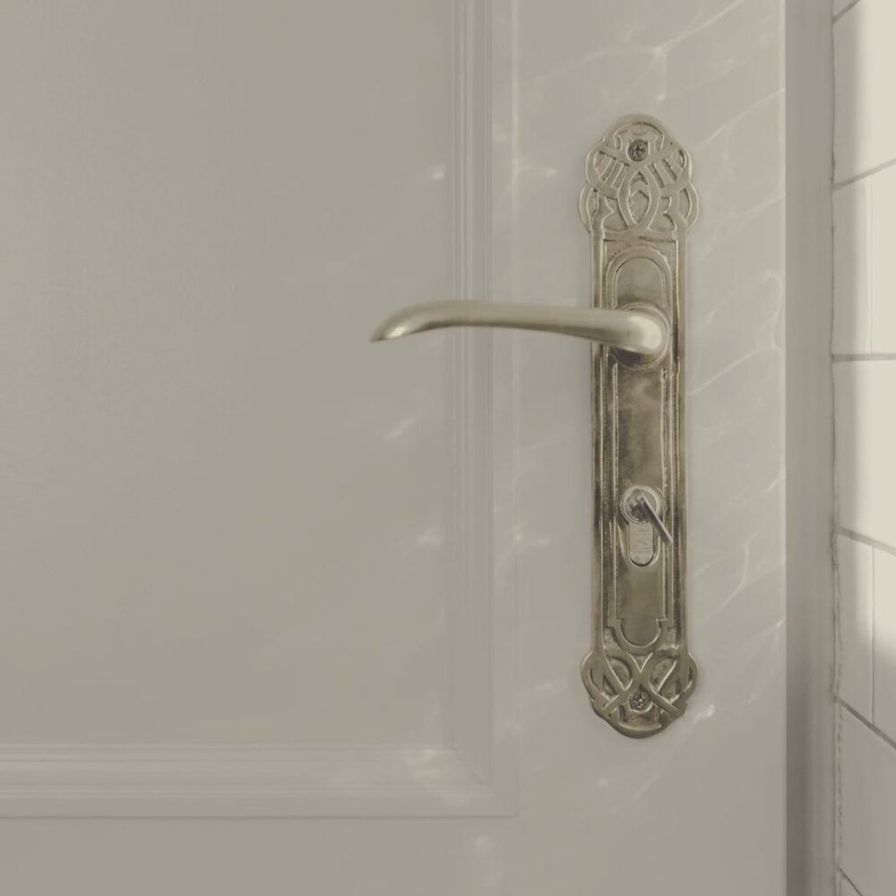 Manilla antigua de latón sobre una puerta blanca, iluminada por la luz de una ventana.