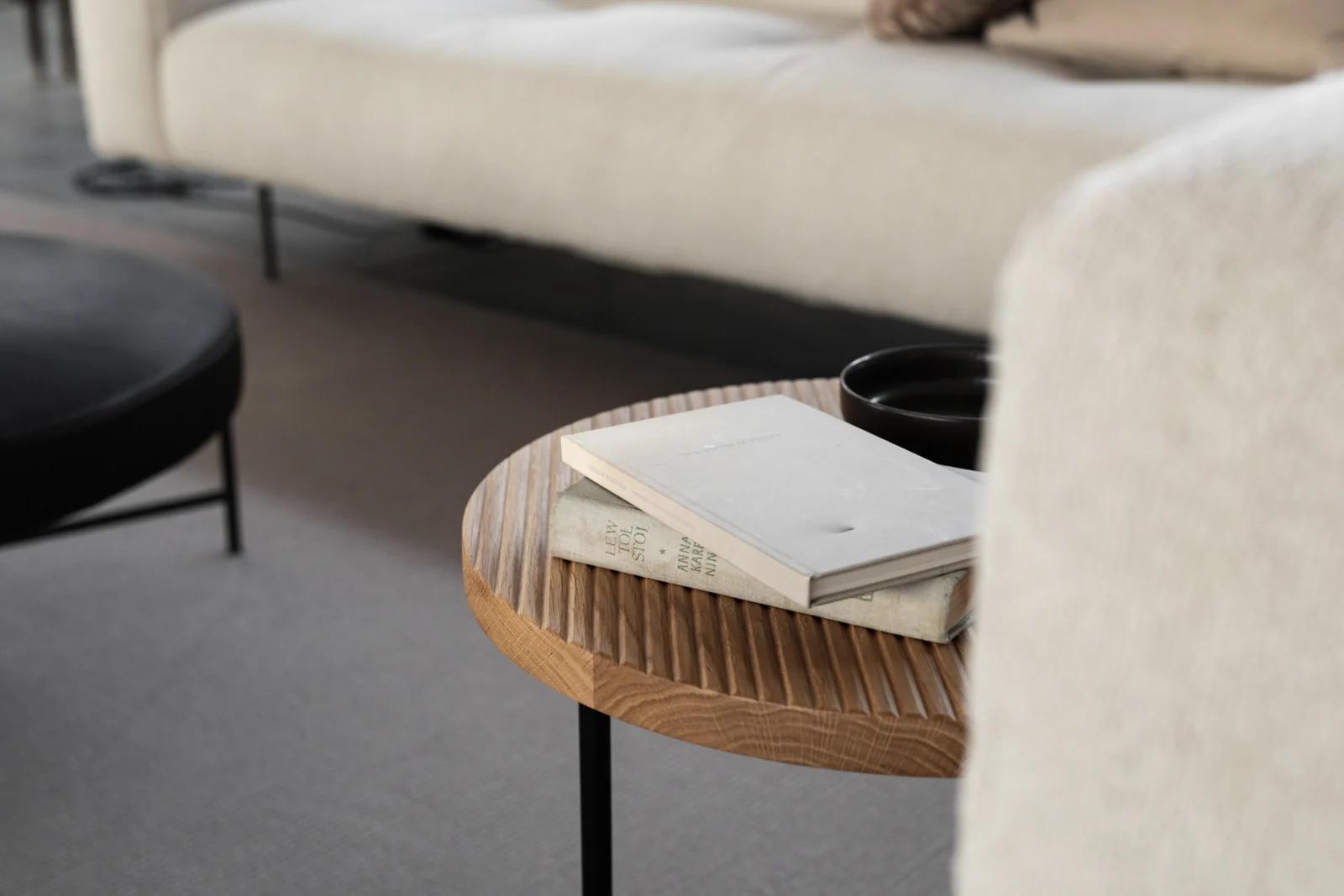 Libros sobre una mesa de roble junto a un sofá de tonos claros.