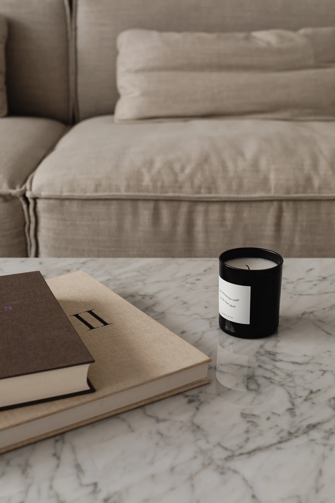 Sofá de lino junto a una mesa de mármol con libros y una vela.