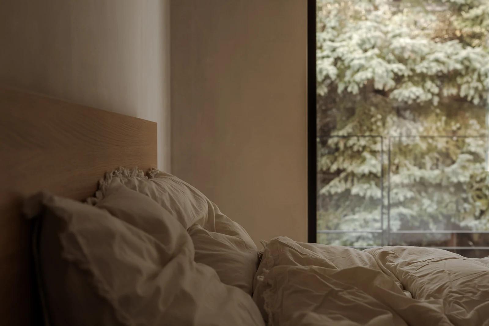 Dormitorio de tonos cálidos con ropa de cama de lino y ventana abierta al verde.