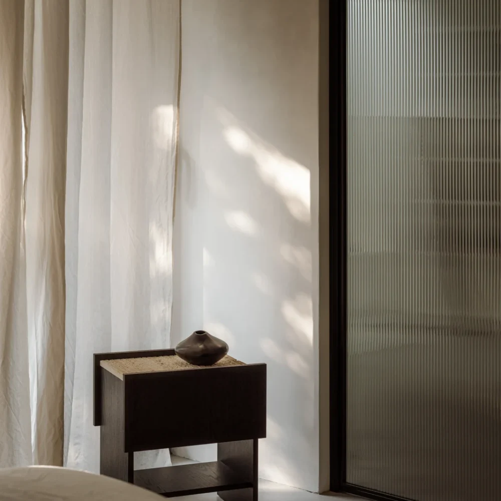 Luz natural sobre cortinas de lino, pared clara y vidrio estriado en un interior de tonos neutros.