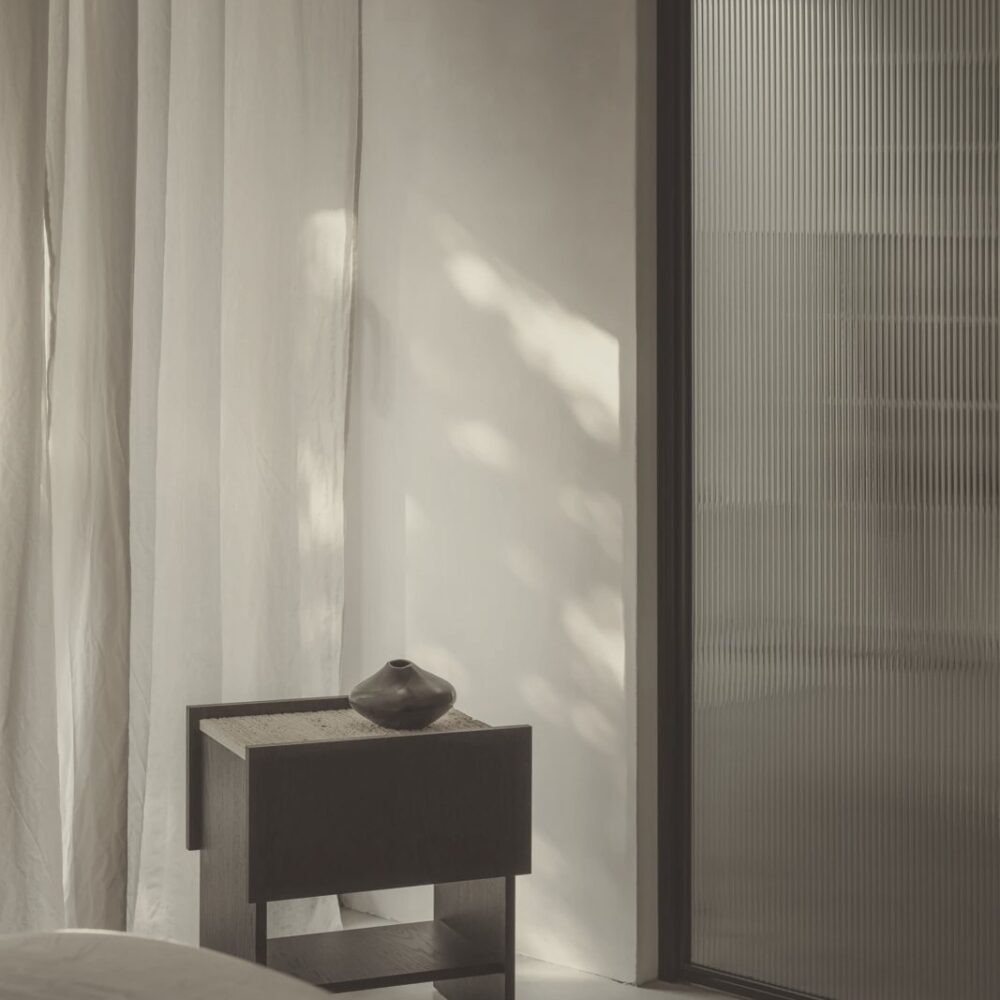 Luz natural sobre cortinas de lino, pared clara y vidrio estriado en un interior de tonos neutros.